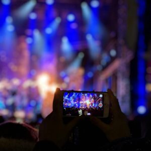 Silhouetted hands holding a smartphone capturing vibrant concert lights.