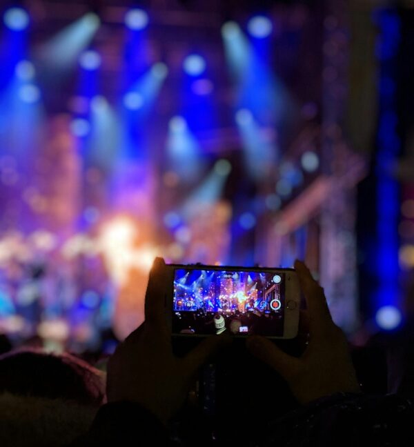 Silhouetted hands holding a smartphone capturing vibrant concert lights.