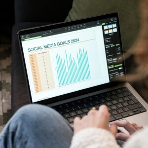 Woman reviewing 2024 social media goals chart on laptop indoors.