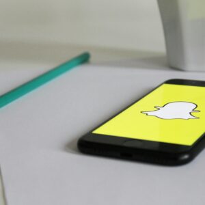 Smartphone with Snapchat logo on a desk with pencil and mug, emphasizing social media and technology.