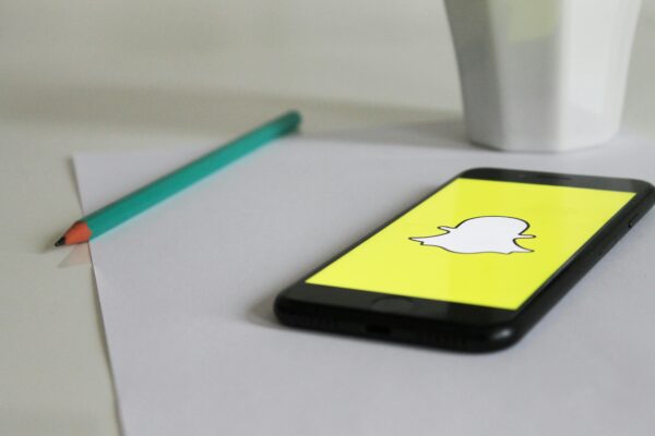 Smartphone with Snapchat logo on a desk with pencil and mug, emphasizing social media and technology.